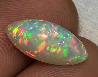 Könnte beinhalten: Ein weißer ovaler Opal-Edelstein mit grünen, orangefarbenen und rosafarbenen Farbschimmern.