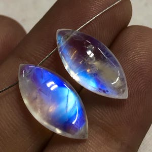 May include: Two iridescent moonstone gemstone beads in a marquise shape. The beads are a milky white colour with blue and purple iridescent flashes.