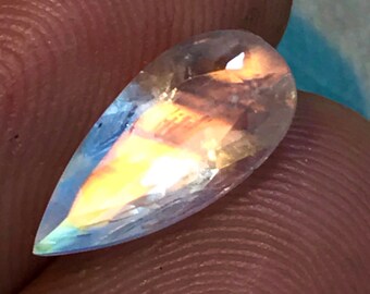 May include: A pearlescent teardrop-shaped gemstone with iridescent rainbow colours, showing a flash of orange and yellow.
