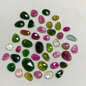 May include: A collection of 30 loose gemstones in various shades of green, pink, and clear. The gemstones are faceted and have a variety of shapes, including oval, round, and pear.