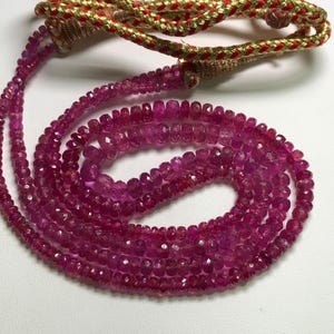 May include: A strand of pink ruby beads, faceted and strung on a cord. The beads are small and uniform in size, creating a delicate and elegant look.