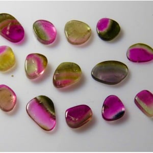 May include: A collection of 14 smooth, polished, oval-shaped gemstones. The stones are a mix of pink, green, and yellow colors.