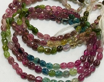 May include: A strand of multi-colored oval-shaped gemstone beads. The beads are a mix of pink, green, blue, and yellow.