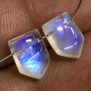 May include: Two iridescent rainbow moonstone beads with a pointed shape, strung on a silver wire.