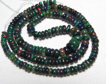May include: A strand of black opal beads with green and red flashes of color. The beads are round and have a smooth, polished finish.