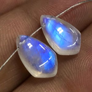 May include: Two teardrop-shaped moonstone beads with iridescent blue and white colours. The beads are strung on a silver wire.