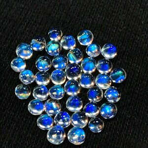 Op de afbeelding: Een verzameling van iriserende blauwe maansteen cabochons, elk met een uniek patroon van licht en kleur.