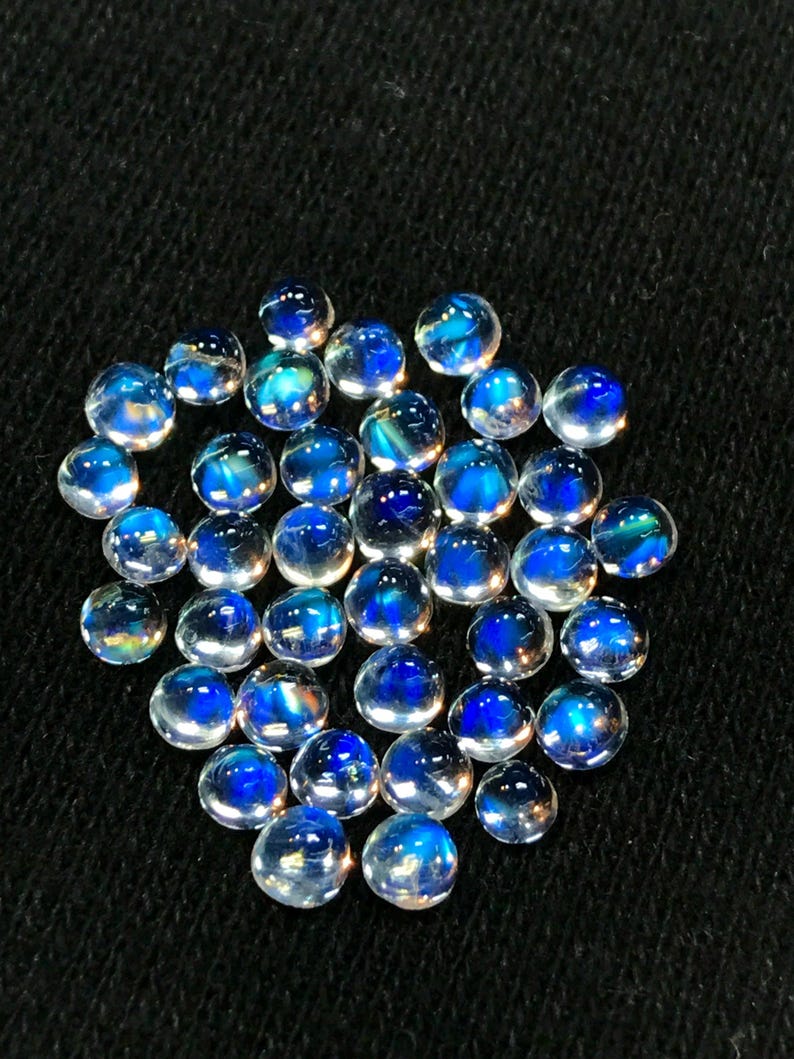 Op de afbeelding: Een verzameling van iriserende blauwe maansteen cabochons, elk met een uniek patroon van licht en kleur.