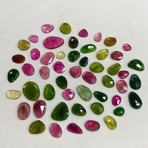 May include: A collection of green, pink, and brown gemstones. The gemstones are faceted and have a variety of shapes and sizes.