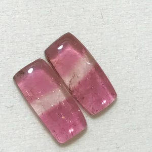 May include: Two pink and white tourmaline gemstones, cut into rectangular shapes.