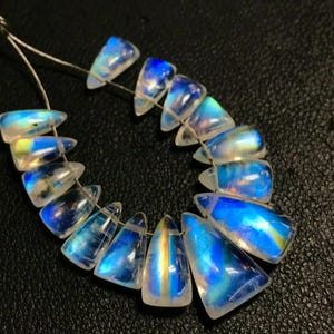 May include: A strand of iridescent rainbow moonstone beads, each bead is a triangular shape with a pointed tip. The beads are strung on a silver wire.