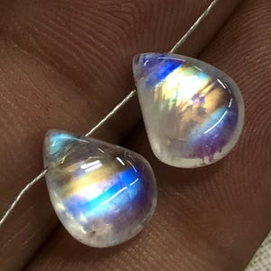 May include: Two teardrop-shaped iridescent moonstone beads with a rainbow sheen. The beads are strung on a silver wire.