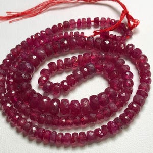 May include: A strand of ruby red gemstone beads. The beads are faceted and have a slightly irregular shape. The beads are strung on a red cord.
