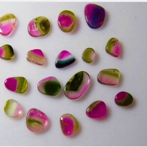 May include: A collection of 17 smooth, polished, multi-colored gemstones. The stones are various shades of pink, green, and purple. They are all roughly oval shaped and have a glossy finish.