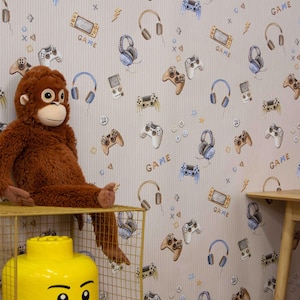 May include: A room with wallpaper featuring a pattern of video game controllers, headphones, and handheld consoles. The word "GAME" is printed on the wallpaper. A brown stuffed monkey sits on a gold wire shelf next to a large yellow Lego head.