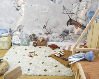 May include: A light blue and white rug with a nautical theme. The rug features a variety of sea creatures, including whales, an octopus, and a crab. There are also stars and a crescent moon on the rug. The rug is in a room with a wooden bed and a wooden chair.