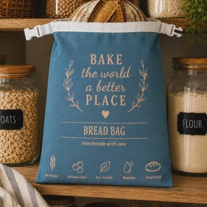 May include: A blue fabric bread bag with a white top closure and buckle. The text reads BAKE the world a better PLACE BREAD BAG Handmade with care. Icons represent No Plastic, Beeswax Lined, Eco-Friendly, Washable, and Keeps Fresh features.