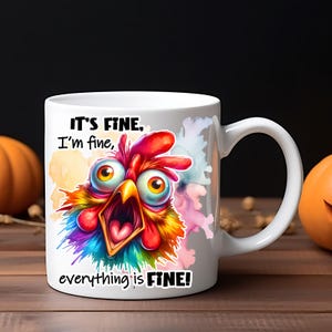 Pode incluir: Uma caneca de cer&acirc;mica branca com uma ilustra&ccedil;&atilde;o de uma galinha de olhos arregalados e plumagem vibrante e multicolorida. O texto "IT'S FINE, I'm fine, everything is FINE!" est&aacute; impresso em letras pretas acima e abaixo do gr&aacute;fico.