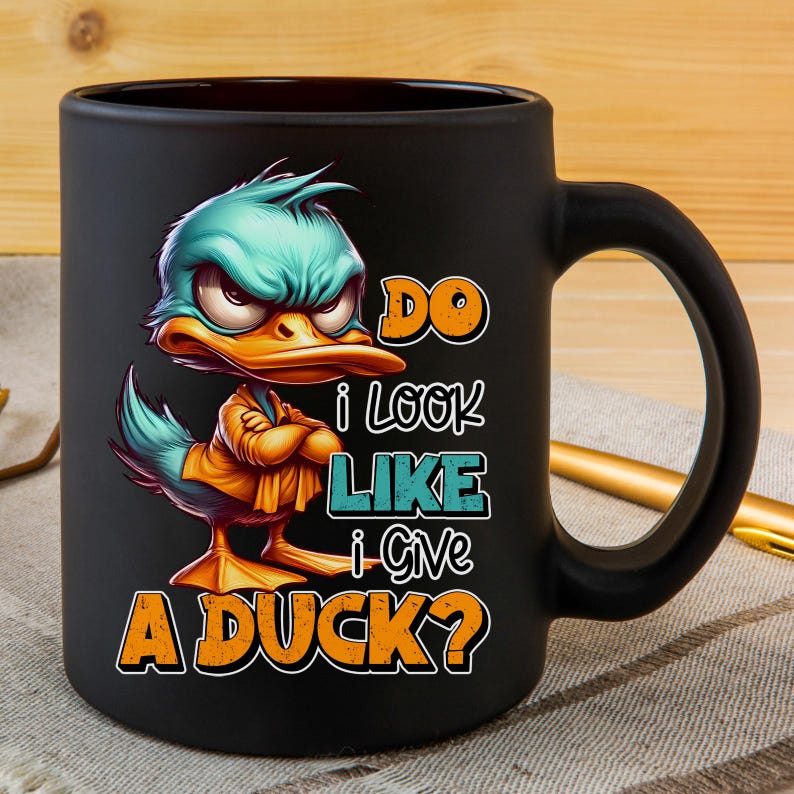 May include: Black ceramic mug featuring a cartoon duck with an angry expression. The duck has teal feathers, an orange beak, and is wearing a yellow shirt. Text on the mug reads "DO I LOOK LIKE I GIVE A DUCK?"