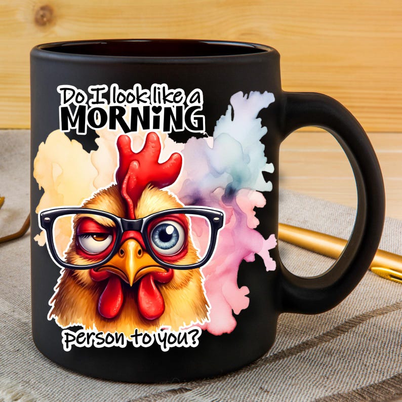 Pode incluir: Uma caneca de cer&acirc;mica preta fosca com um gr&aacute;fico colorido de uma galinha usando &oacute;culos de aro preto. O texto diz: Do I look like a MORNING person to you? A galinha tem uma crista e barbelas vermelhas, com um olho semicerrado e outro aberto.