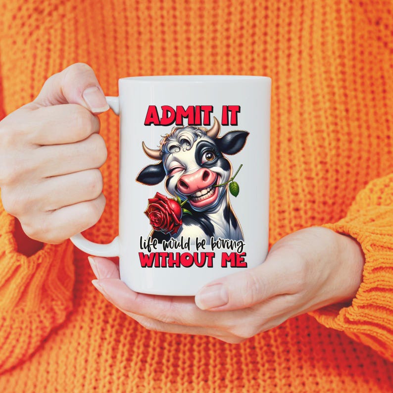 May include: White ceramic mug featuring a cartoon cow winking and holding a red rose. The mug has the text "ADMIT IT" above the cow and "life would be boring WITHOUT ME" below. The mug is held by a person wearing an orange sweater.