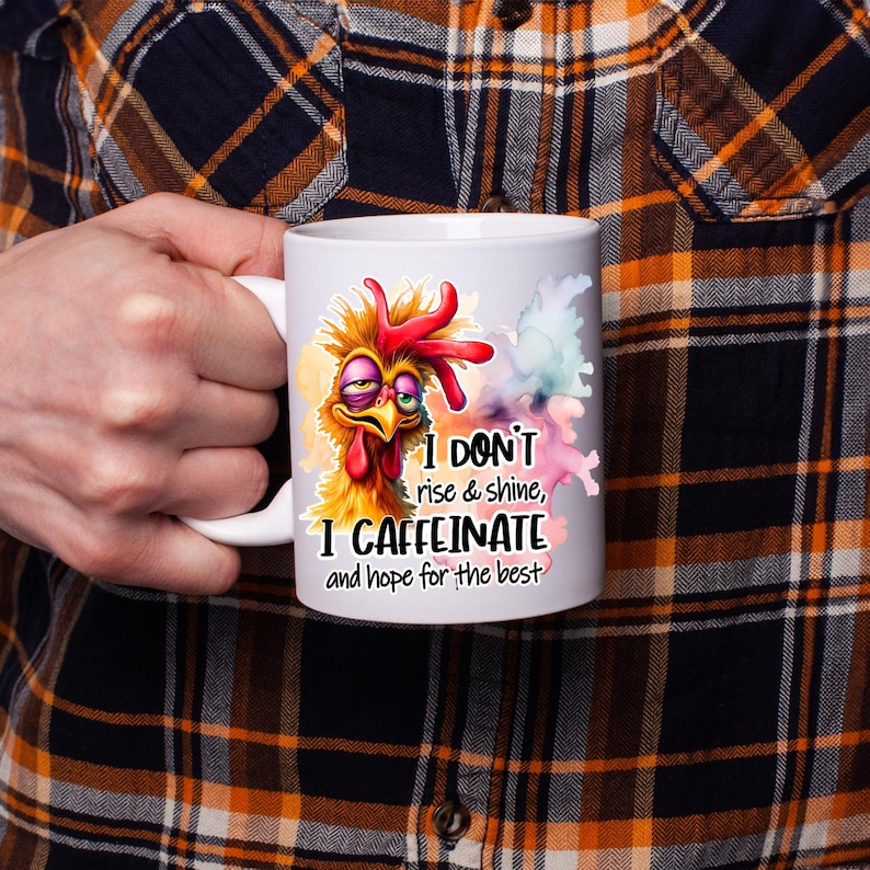 Pode incluir: Uma caneca de cer&acirc;mica branca com uma ilustra&ccedil;&atilde;o colorida de uma galinha despenteada e sonolenta com penas bagun&ccedil;adas. O texto diz: I DON'T rise & shine, I CAFFEINATE and hope for the best. O design inclui salpicos de cor estilo aguarela.