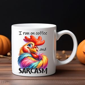 May include: White ceramic mug with a colorful rooster illustration and the text "I run on coffee and SARCASM." The rooster features vibrant red, blue, yellow, and purple feathers. The mug has a curved handle and is set against a wooden surface.