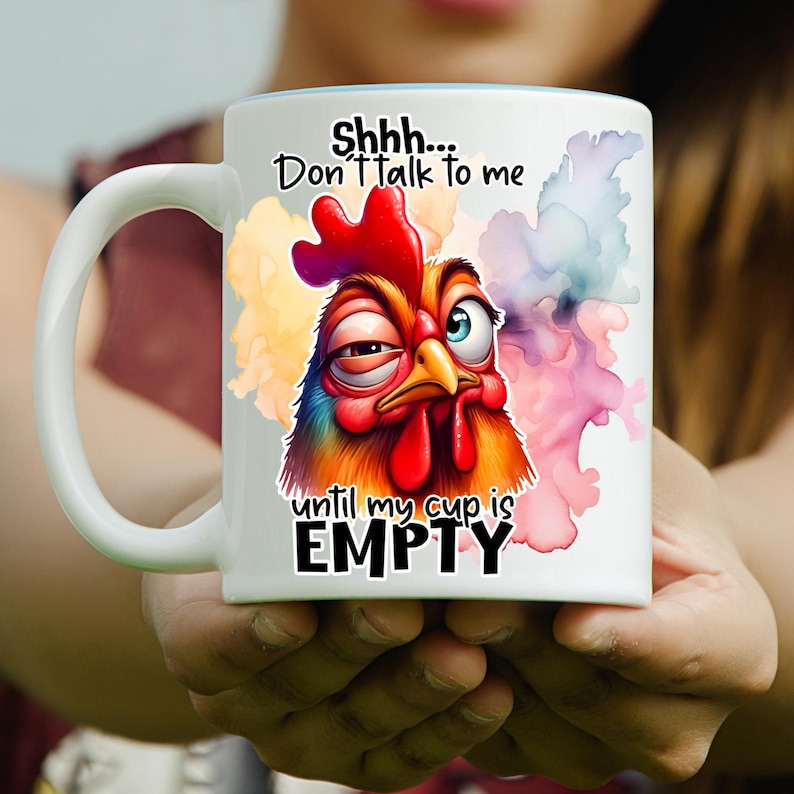 Pode incluir: Uma caneca de cer&acirc;mica branca com uma ilustra&ccedil;&atilde;o colorida de uma galinha rabugenta com um olho semicerrado e o outro bem aberto. O texto diz Shhh... Don't talk to me until my cup is EMPTY, rodeado por salpicos de aguarela abstratos.