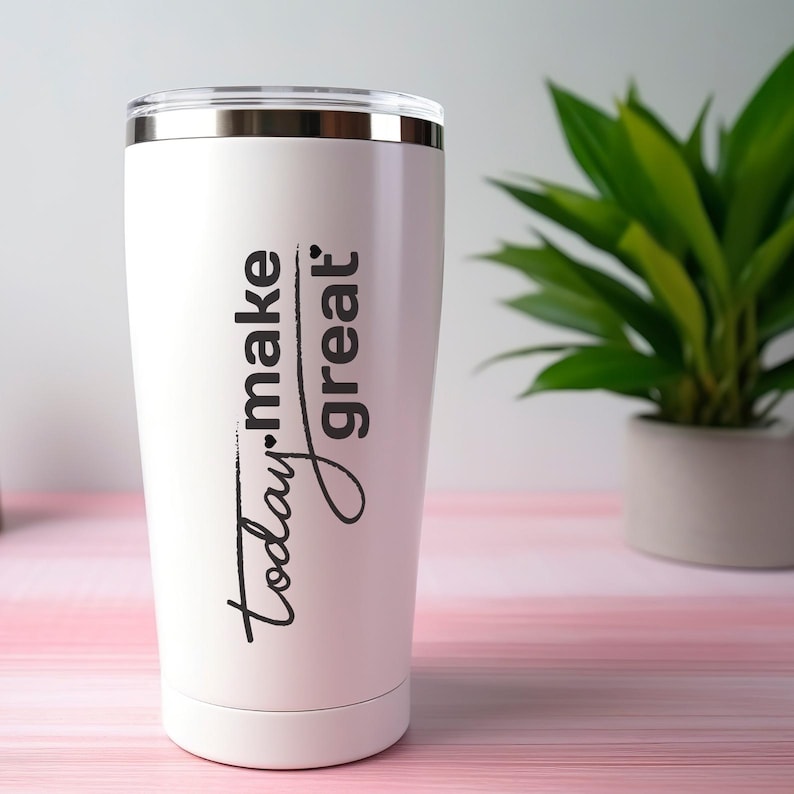 May include: A white insulated travel mug with a silver rim and lid. The mug has the words "Today. make great" in black script. A green plant in a white pot is in the background.