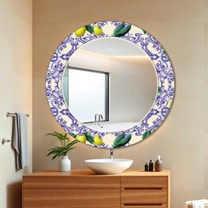 May include: A round decorative mirror with a patterned border featuring blue and white swirls, green leaves, and yellow lemons. The mirror is mounted above a wooden vanity with a white sink in a bathroom setting.