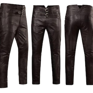 May include: Dark brown leather trousers featuring a high-waisted design with two horizontal straps across the front, each secured by a silver-toned metal buckle. The trousers are shown from three angles, displaying a slim-fit silhouette and stitching.
