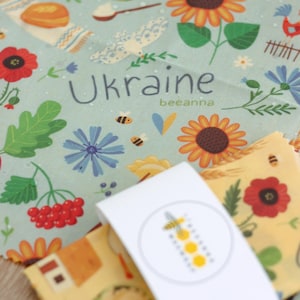 May include: A set of three beeswax food wraps with a blue and yellow floral design. The wraps feature sunflowers, bees, and the word "Ukraine" with the text "beeanna".