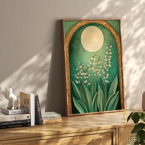 May include: A framed art print featuring a botanical illustration of lily of the valley flowers. The artwork has a green and gold color scheme, with a large moon in the background. The print is displayed on a wooden cabinet with books and decorative items.