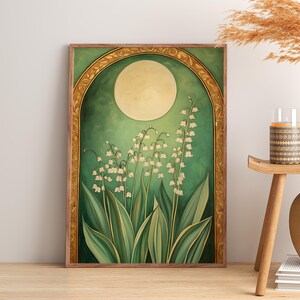 May include: A framed art print featuring a botanical illustration of lily of the valley flowers. The artwork has a green and gold color scheme, with a large moon in the background. The print is displayed on a wooden floor.
