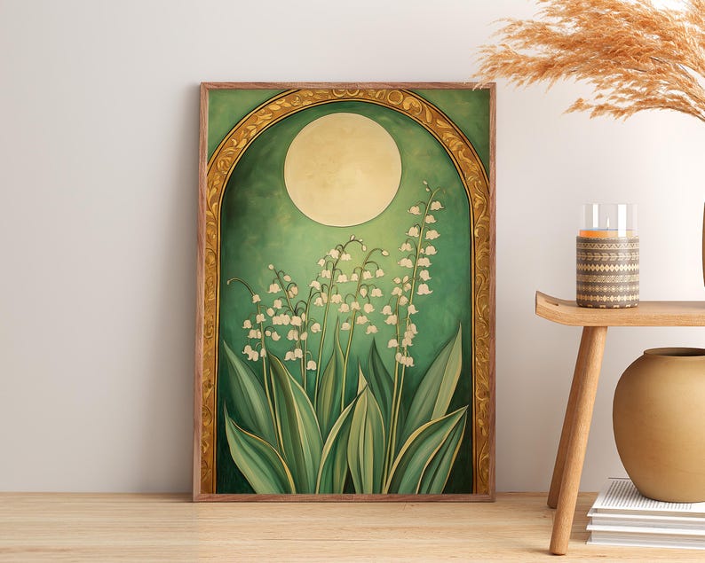 May include: A framed art print featuring a botanical illustration of lily of the valley flowers. The artwork has a green and gold color scheme, with a large moon in the background. The print is displayed on a wooden floor.