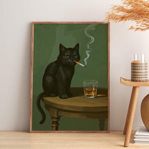 Op de afbeelding: Een ingelijste kunstdruk toont een zwarte kat met groene ogen die een sigaret rookt. Een glas amberkleurige vloeistof staat naast de kat op de tafel. De achtergrond is effen groen.