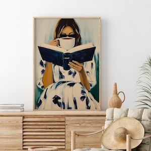 May include: A framed art print depicts a person wearing sunglasses, reading a book, and drinking from a white mug. The person is wearing a white dress with blue floral patterns. The book has a dark blue cover.