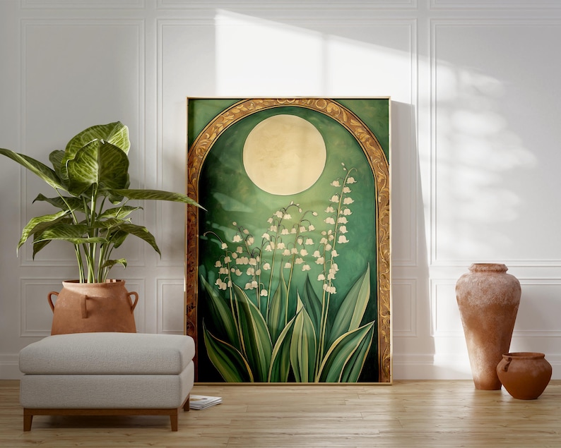 May include: A framed art print featuring a stylized depiction of lily of the valley flowers under a full moon. The artwork has a green and gold color scheme, with a large, round moon and detailed floral elements. The print is displayed in a room with a plant and decorative vases.
