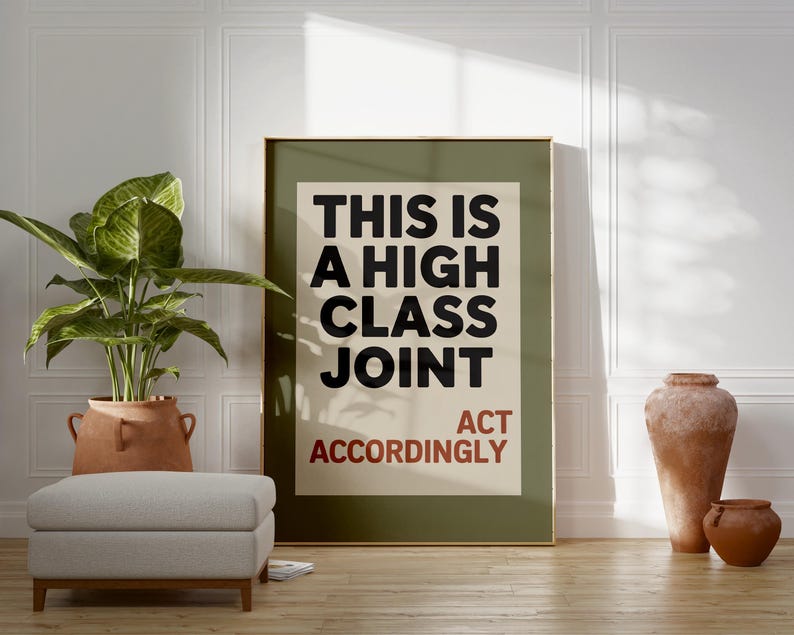 May include: A framed poster with the text "THIS IS A HIGH CLASS JOINT ACT ACCORDINGLY" in black and red. The poster is in a room with a plant in a terracotta pot, a gray ottoman, and decorative vases.