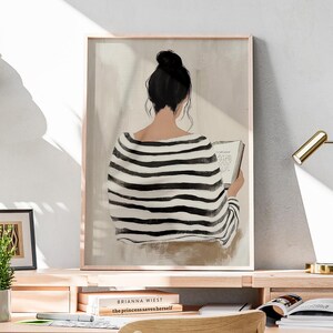 May include: A black and white striped shirt with a woman reading a book. The woman has dark hair pulled back in a bun. The background is a light beige color.