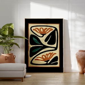 May include: Abstract floral art print in a black frame. The artwork features orange flowers, black leaves, and a cream background. The framed art is displayed in a room with a neutral colour palette, a potted plant, and a grey ottoman.