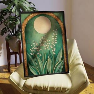 May include: A framed art print featuring a stylized illustration of lily of the valley flowers. The artwork has a green and gold color scheme with a large moon in the background. The print is displayed on a cream-colored chair.