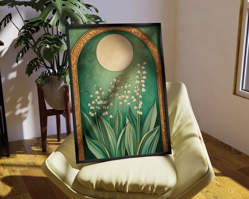 May include: A framed art print featuring a stylized illustration of lily of the valley flowers. The artwork has a green and gold color scheme with a large moon in the background. The print is displayed on a cream-colored chair.