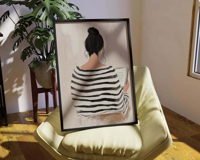 May include: A framed illustration of a person sitting and reading a book. The person is wearing a black and white striped shirt and has dark hair. The background is a light beige color.
