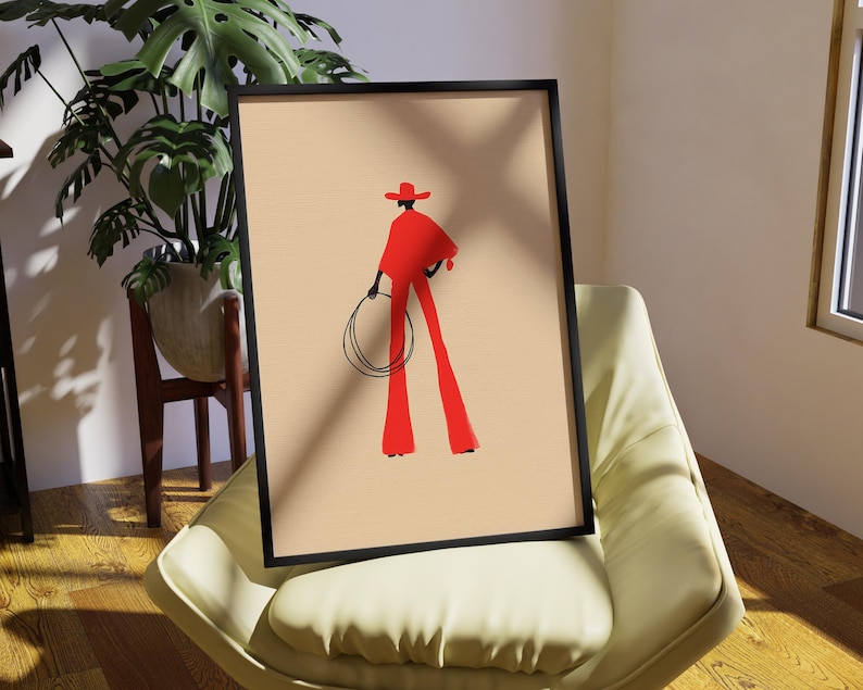 May include: Framed art print featuring a stylized illustration of a figure in red attire, including a hat and flared pants, holding a lasso. The artwork is set against a beige background within a black frame, creating a bold visual statement.