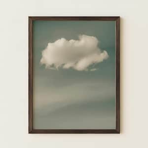May include: A rectangular wall art print featuring a single white cloud centred against a muted, soft teal and grey sky. The artwork is enclosed in a dark brown wooden frame with a thin profile, creating a clean and simple display for the image.
