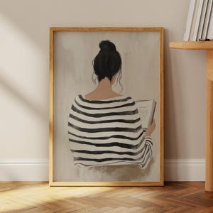 May include: A framed illustration of a person wearing a black and white striped shirt, sitting and reading a book. The person's back is facing the viewer. The background is a light beige color.