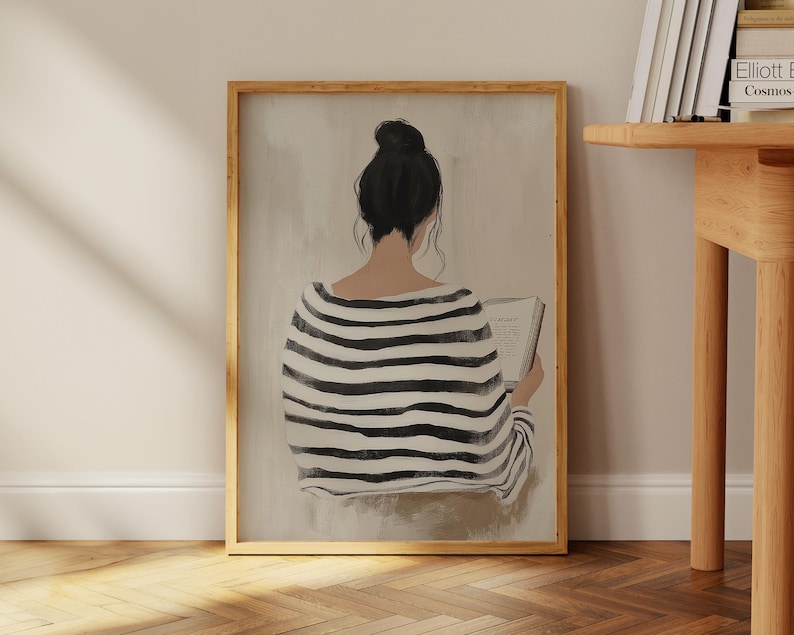 May include: A framed illustration of a person wearing a black and white striped shirt, sitting and reading a book. The person's back is facing the viewer. The background is a light beige color.