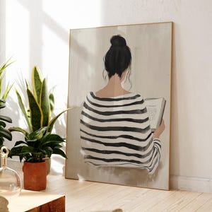 May include: A black and white striped shirt with a woman sitting and reading a book. The woman has her back to the viewer and her hair is pulled back in a bun. The background is a light beige color.
