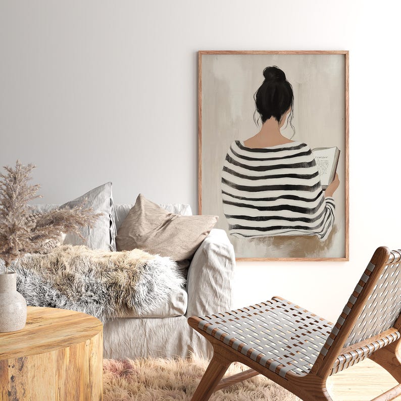 May include: A black and white striped illustration of a person sitting and reading a book. The illustration is framed in a light wood frame and is set against a light beige background.